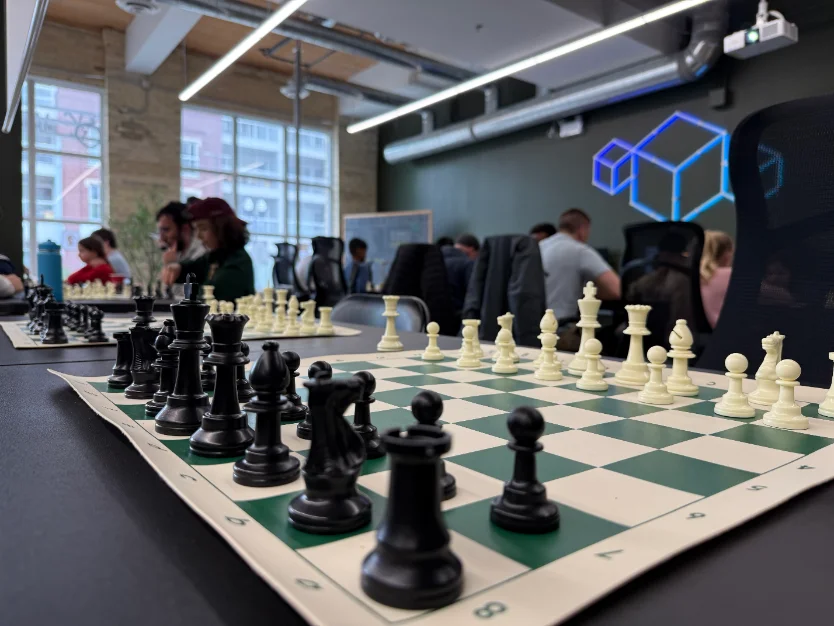 A chess board set up at the Vector Space Chess Club, players in the background